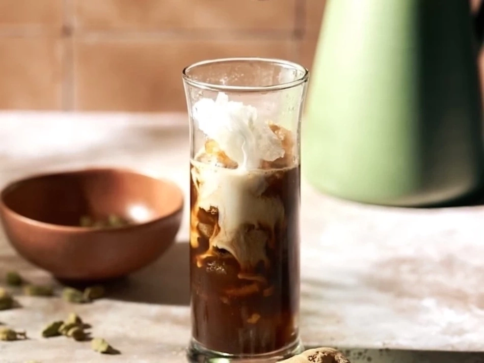 Ein Glas Kaffee mit Sahne, daneben eine Schale mit Gewürzen und ein grüner Krug.