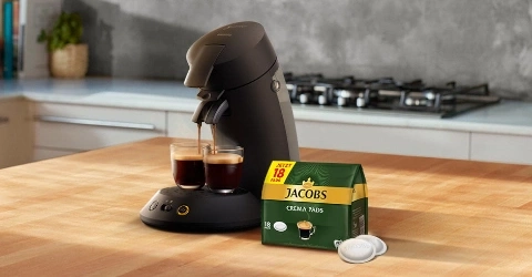 Kaffeemaschine mit Jacobs Crema Pads auf einer Holzoberfläche in einer Küche.