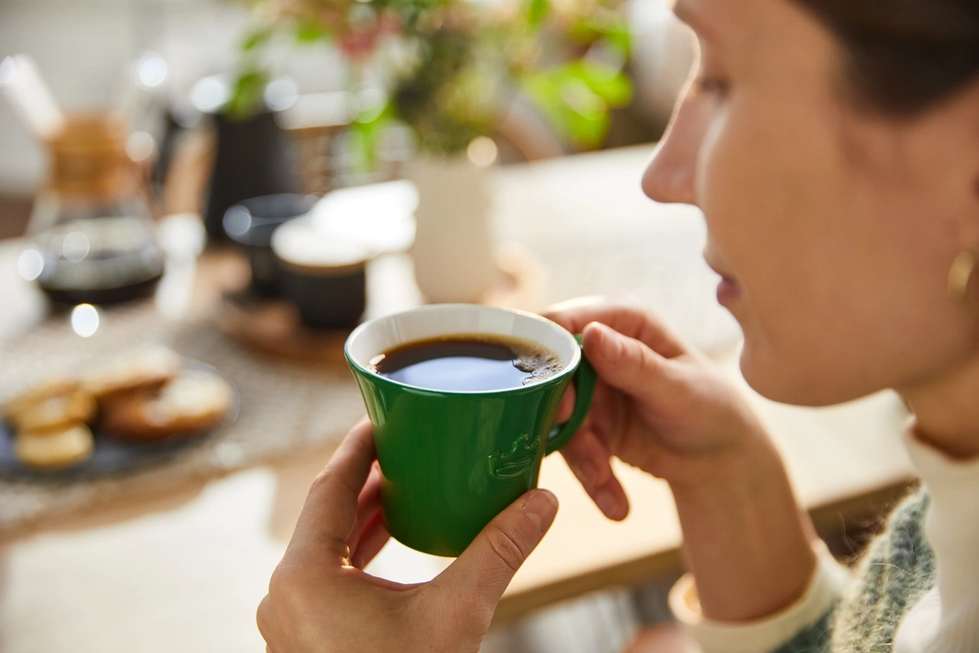 Person trinkt Kaffee aus einer grünen Tasse, Nahaufnahme, entspannt, gemütlich, Morgen