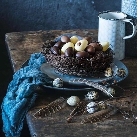 Osternest mit Eiern, Federn und Tasse auf einem Holztisch