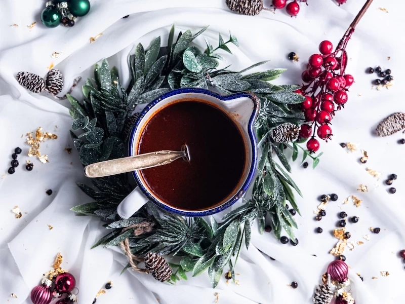Festliches Getränk in einer Tasse, umgeben von Dekorationen und Beeren.