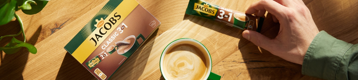 Jacobs 3-in-1 Classic Kaffee, Tasse, Packung, Hand, Holzoberfläche, Nahaufnahme