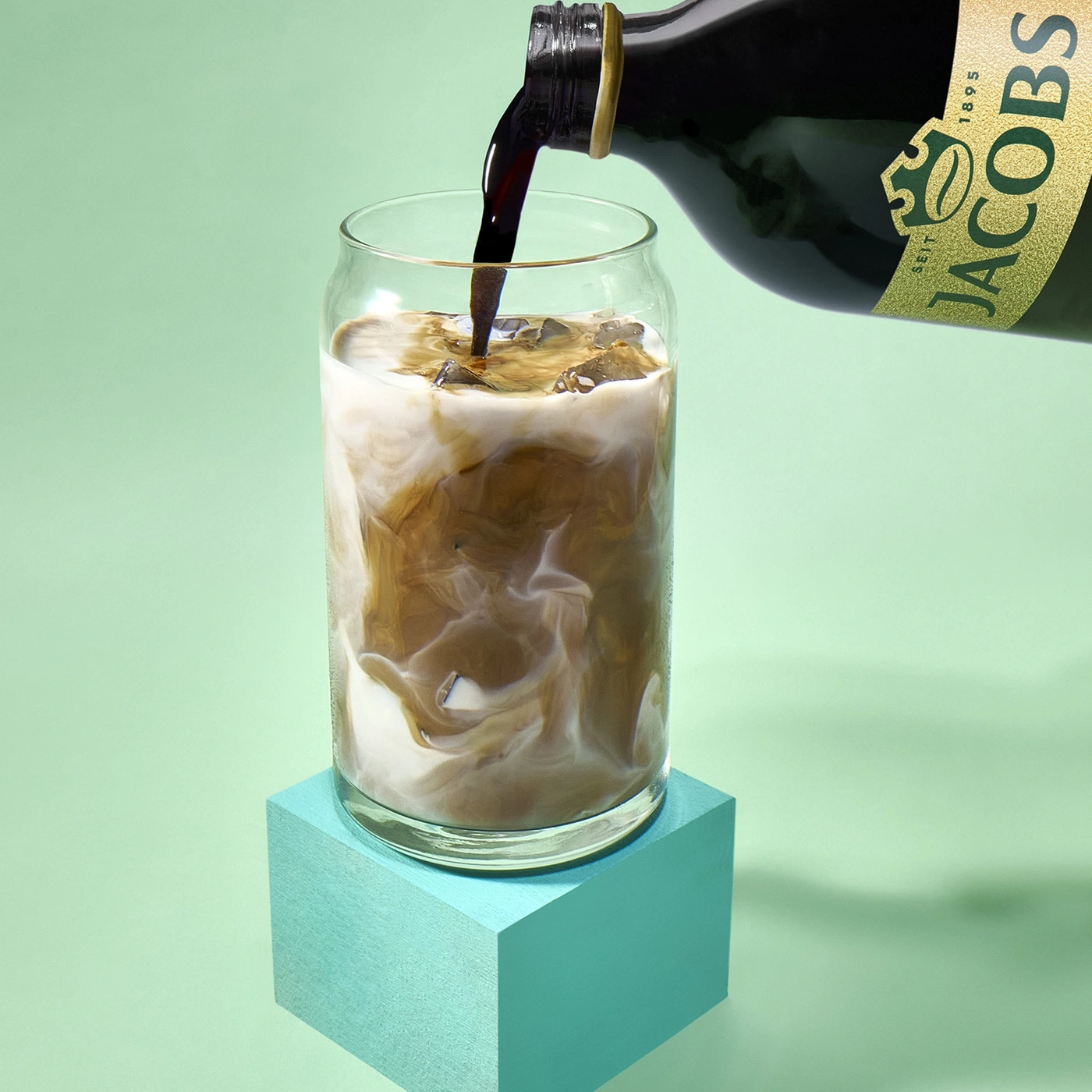 Kaffee wird in ein Glas mit Eis und Milch gegossen.