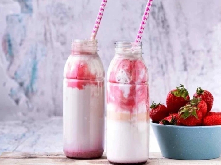 Zwei Erdbeer-Smoothies mit Strohhalmen und Erdbeeren in einer Schüssel.