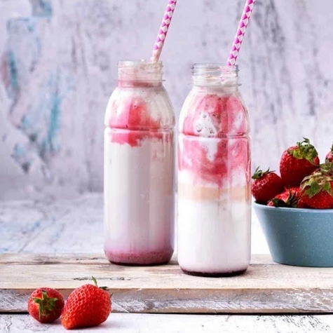 Zwei Erdbeer-Smoothies in Flaschen mit Strohhalmen und Erdbeeren