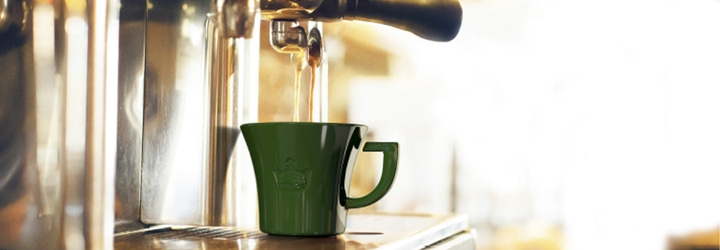Kaffee wird in eine grüne Tasse gegossen, die sich unter einer Kaffeemaschine befindet.