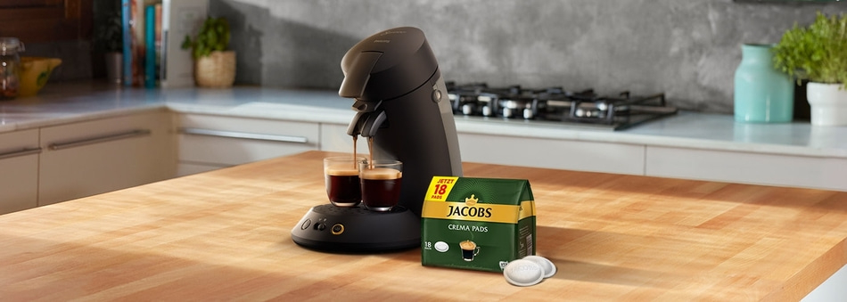 Kaffeemaschine mit Jacobs Crema Pads auf einer Holzoberfläche in einer Küche.
