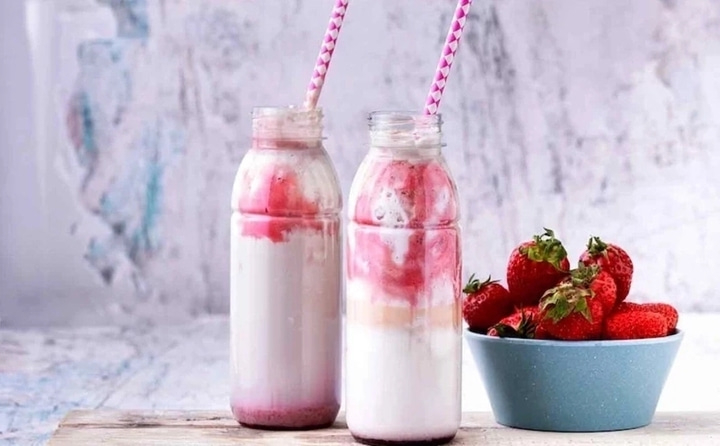 Zwei Erdbeer-Smoothies mit Strohhalmen und Erdbeeren in einer Schüssel.