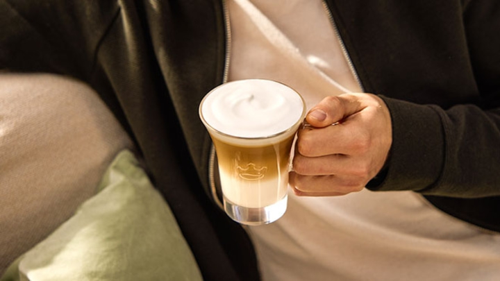 Person hält ein Glas Latte Macchiato mit Milchschaum in der Hand