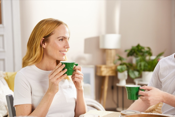 Frau trinkt Kaffee, lächelt, grüne Tasse, Tisch, Person, Innenraum, hell