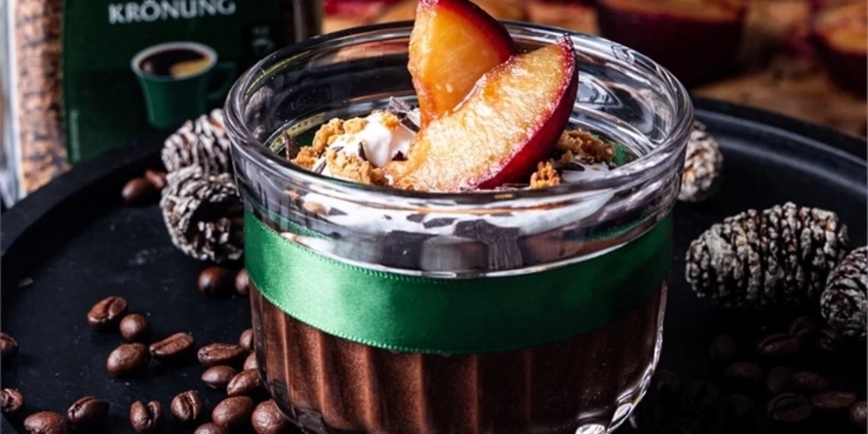Dessert im Glas mit Pflaume, Kaffeebohnen und Tannenzapfen auf schwarzem Tablett