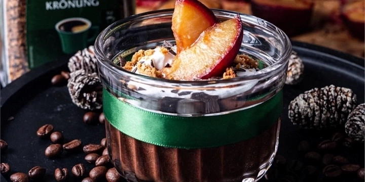 Dessert im Glas mit Pflaume, Kaffeebohnen und Tannenzapfen auf schwarzem Tablett