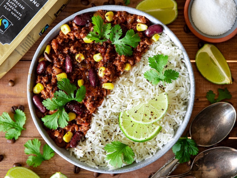 Schüssel mit Chili, Reis, Limette und Koriander auf Holzuntergrund