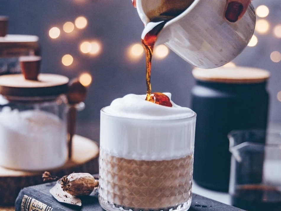 Kaffee mit Sahne, Sirup wird in ein Glas gegossen, Bokeh-Effekt im Hintergrund
