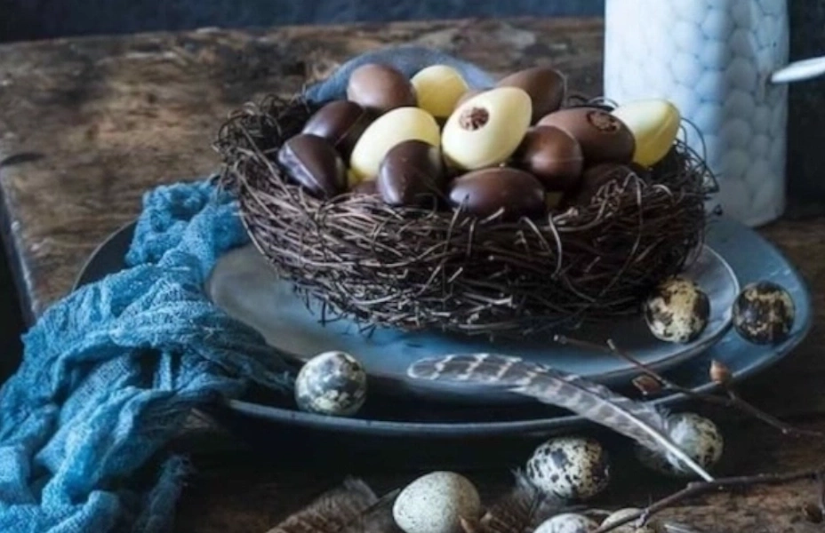 Osternest mit Schokoladeneiern und Wachteleiern auf einem Teller mit Federn