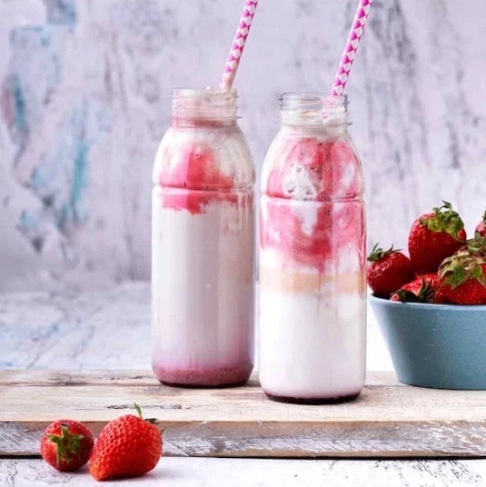 Zwei Erdbeer-Smoothies in Flaschen mit Strohhalmen und Erdbeeren