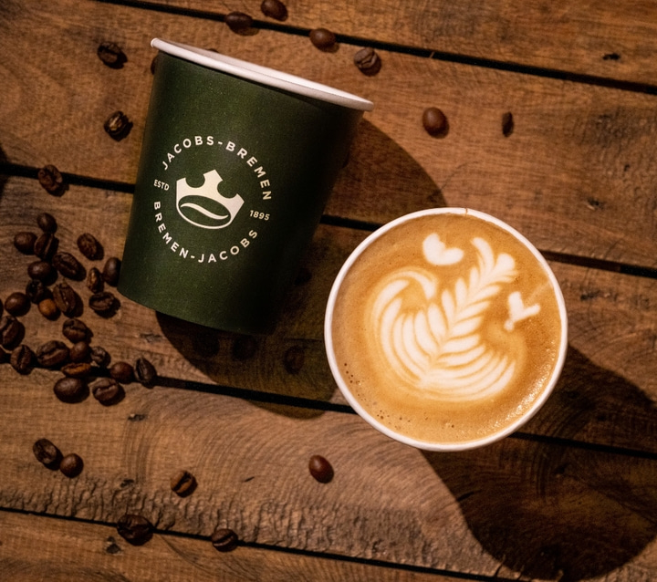 Kaffeebecher mit Latte Art und Kaffeebohnen auf Holzuntergrund