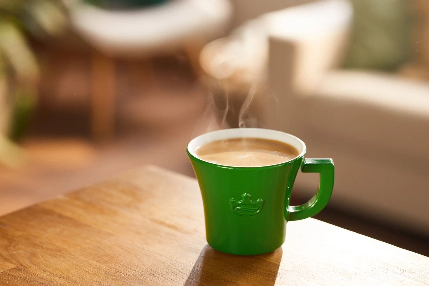 Grüner Kaffeebecher mit heißem Kaffee auf einem Holztisch, Dampf steigt auf.