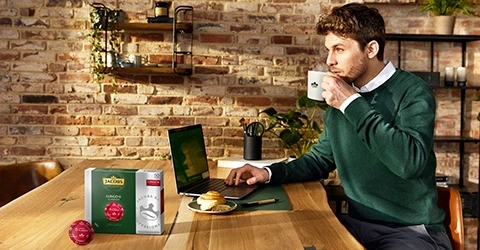 Mann trinkt Kaffee am Laptop, Jacobs Kaffeeprodukte auf dem Tisch.